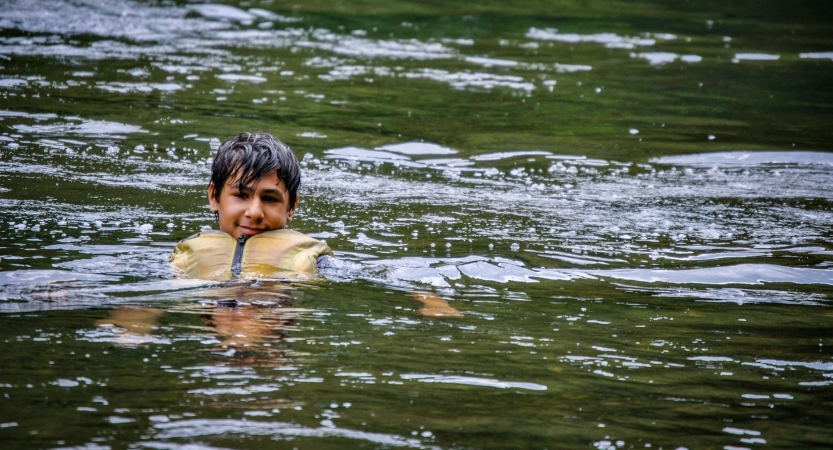 a person wearing a life jacket smiles as they float in calm water. 